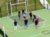 Seven people stand on a small outdoor sports court, some playing with a football.